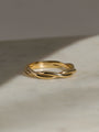 Twisted yellow gold band resting on a light marble surface with soft shadows.