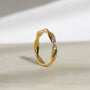 Yellow gold twist band ring with a row of diamonds on one side, vertical tilted angle to showcase the design of the entire band. Photographed on a light beige surface with a soft shadow.