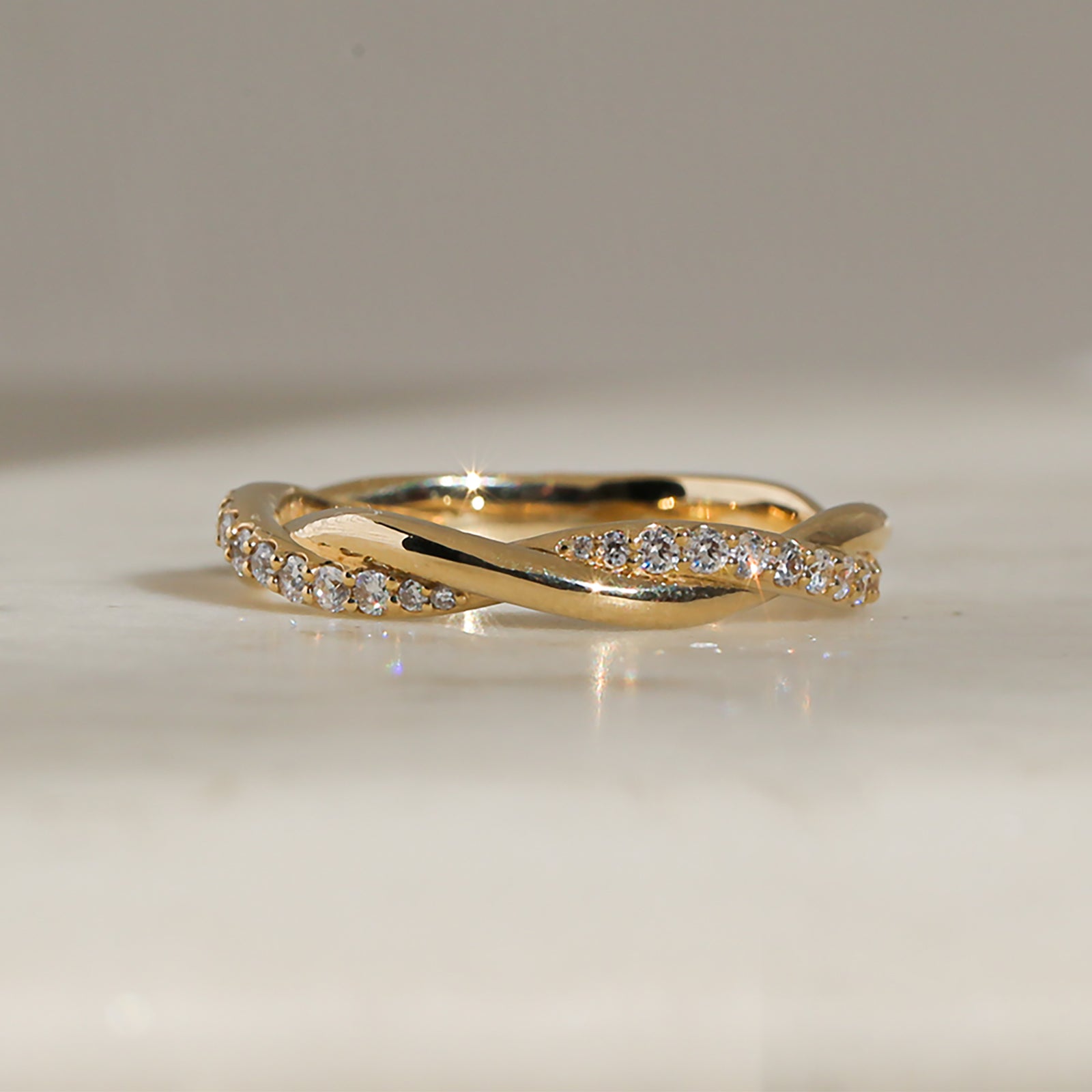 Yellow gold ring with a twisted band design, featuring rows of gold, one lined with diamonds.
