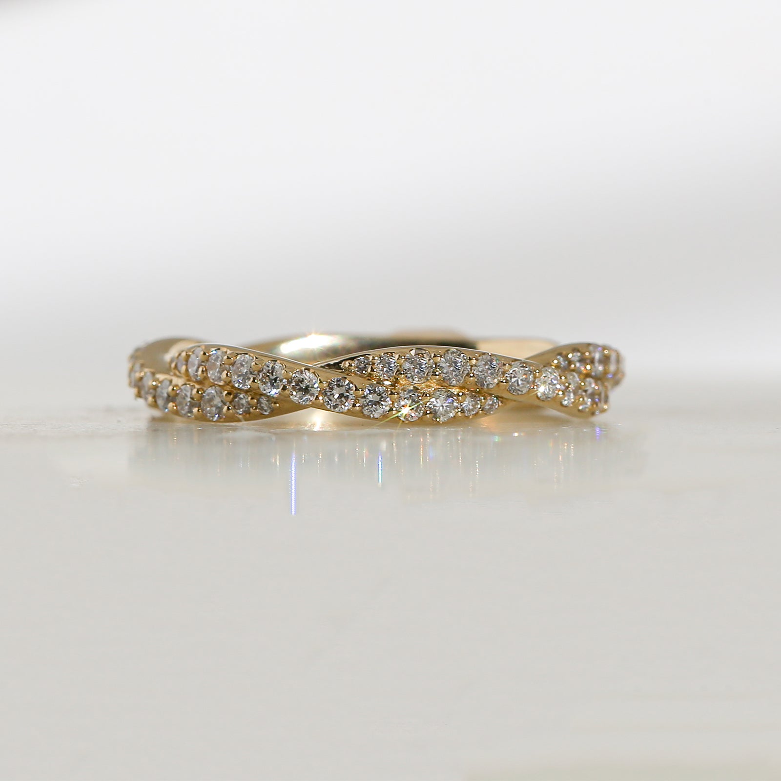 Yellow gold band featuring two twisted rows of small pavé diamonds, photographed on a clean white semi-reflective surface.