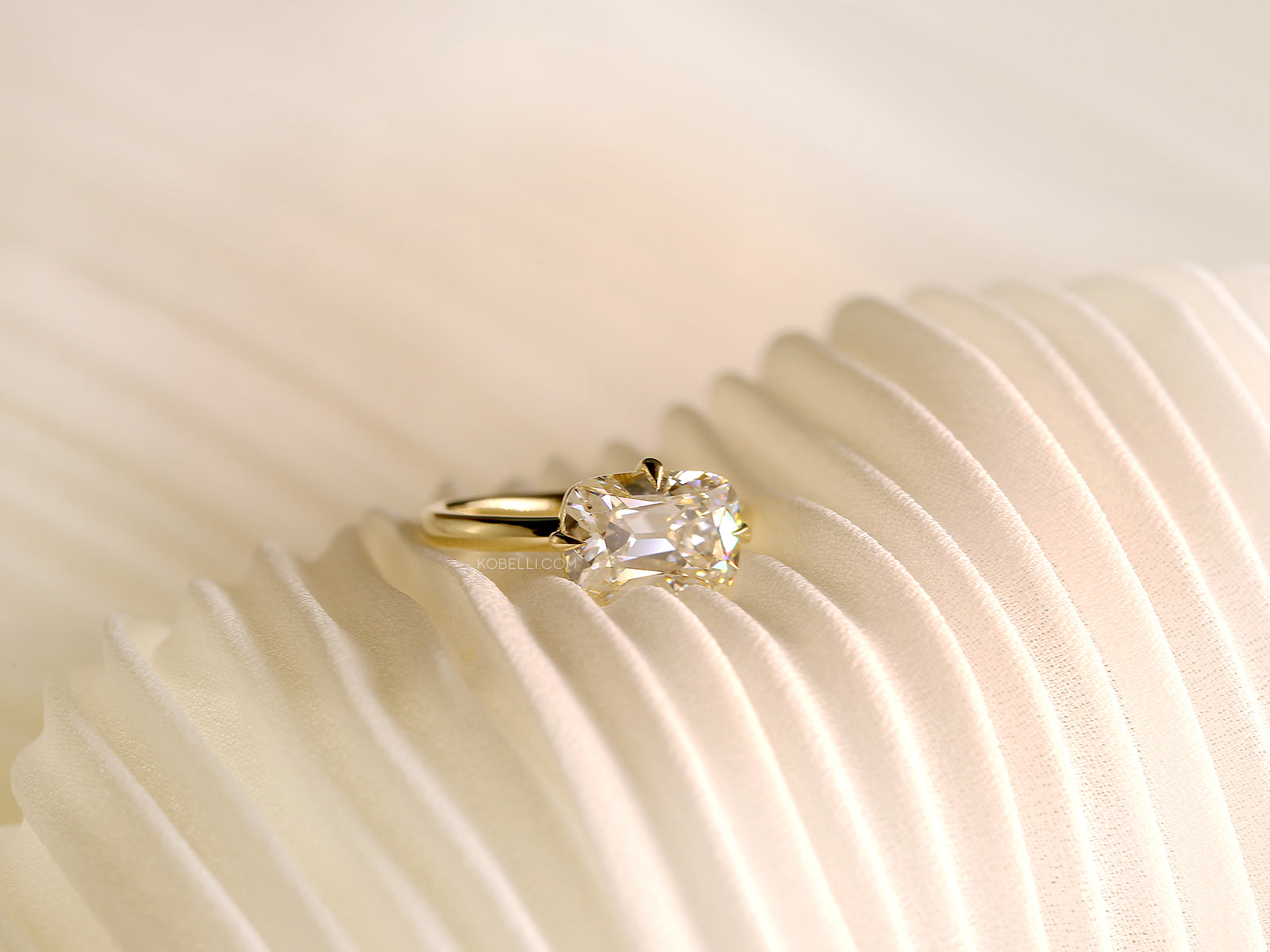 lifestyle image of Kobelli's east-west old mine cut diamond ring sitting atop a pleated white fabric