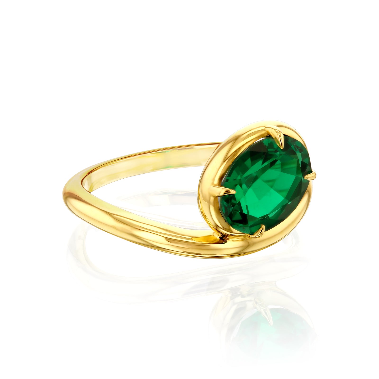 A gold ring featuring a large, oval-cut green emerald gemstone in a bezel-prong setting known as collet, shown on a clean white background with a soft reflection below.