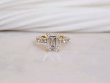 Four prongs carry the emerald-cut center diamond