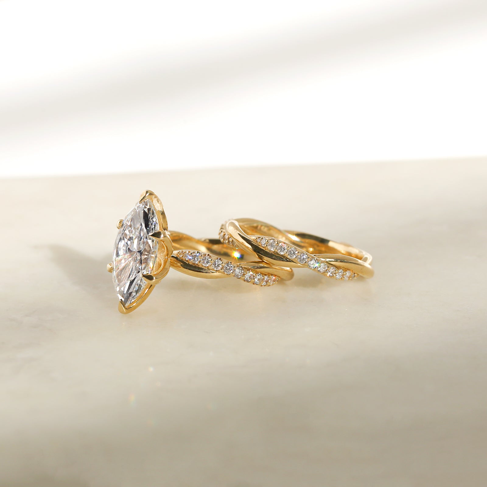 3.25 Carat Lab Grown Diamond Marquise Shifting Helix Ring paired to the Shifting Helix Wedding Band Ring - side angle resting on a white table