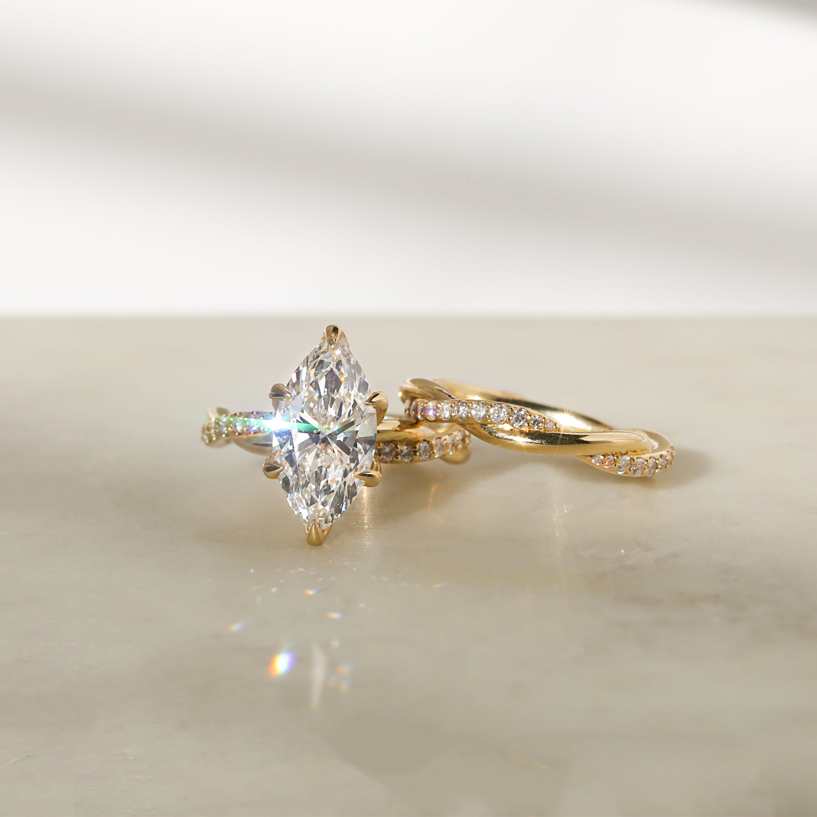 3.25 Carat Lab Grown Diamond Marquise Shifting Helix Ring paired to the Shifting Helix Wedding Band Ring - front angle resting on a white table