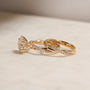side angle of the 3.25 Carat Lab Grown Diamond Round Shifting Helix Ring paired with the Shifting Helix Wedding Band Ring, leaning against the bottom edge of the engagement ring - yellow gold option resting on an off-white table with subdued daylight