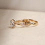 side angle of the 3.25 Carat Lab Grown Diamond Round Shifting Helix Ring paired with the Plain Helix Wedding Band Ring, leaning against the bottom edge of the engagement ring - yellow gold option resting on an off-white table with subdued daylight