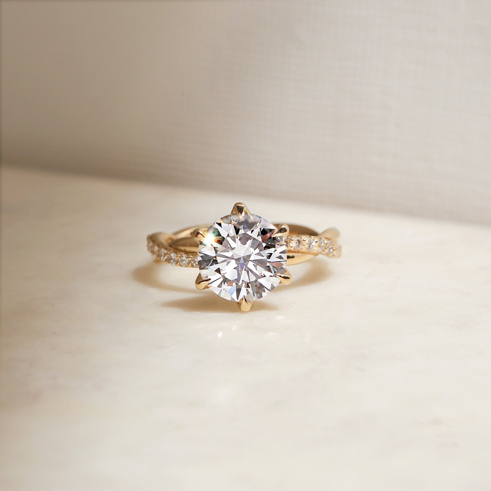 3.25 Carat Lab Grown Diamond Round Shifting Helix Ring - lifestyle image of yellow gold option resting on an off-white table with subdued daylight