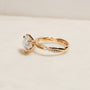 3.25 Carat Lab Grown Diamond Round Shifting Helix Ring - lifestyle image of yellow gold option resting on an off-white table with subdued daylight, photographed at a side angle slightly above the ring to show depth and details