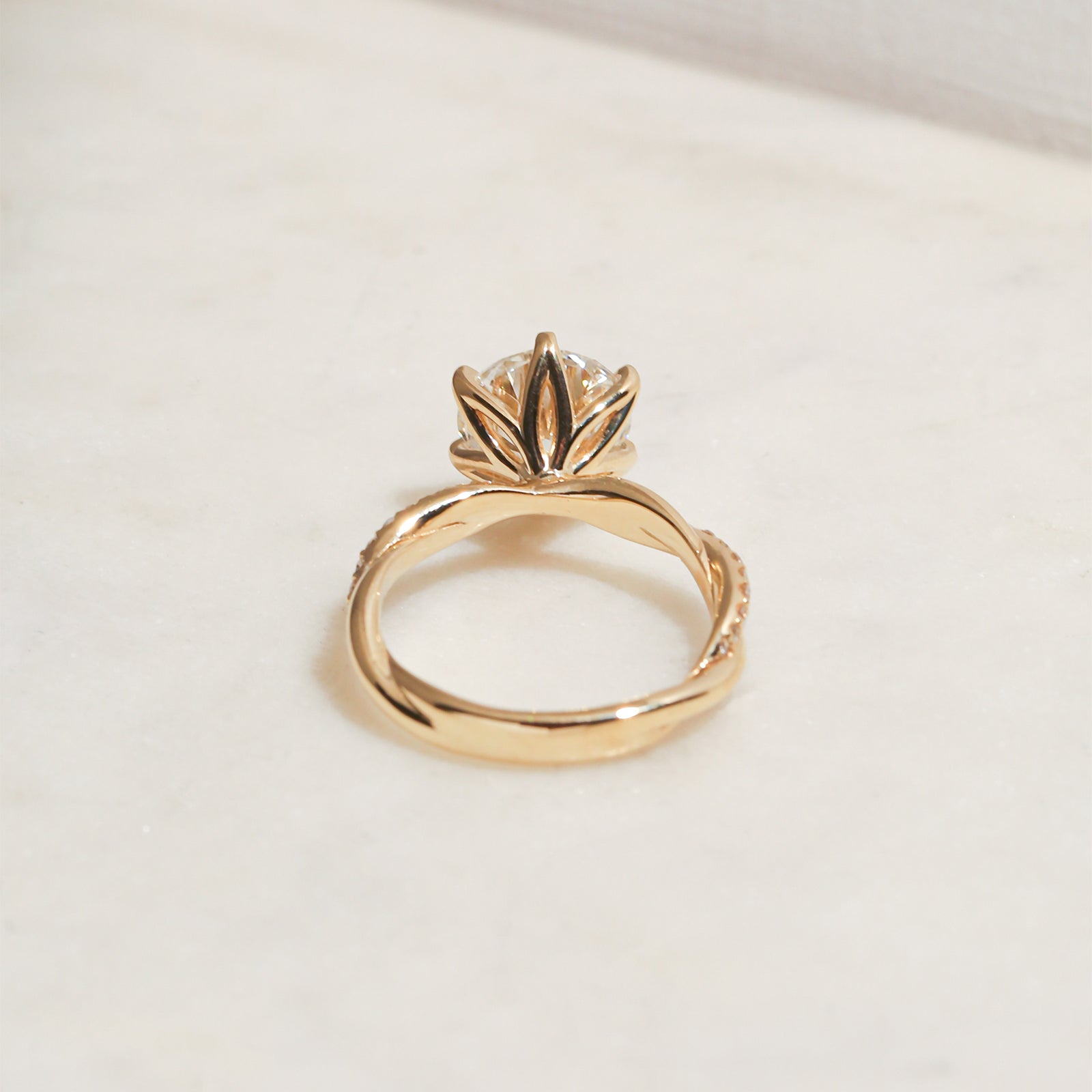 3.25 Carat Lab Grown Diamond Round Shifting Helix Ring - lifestyle image of yellow gold option resting on an off-white table with subdued daylight, photographed at a back angle of the ring