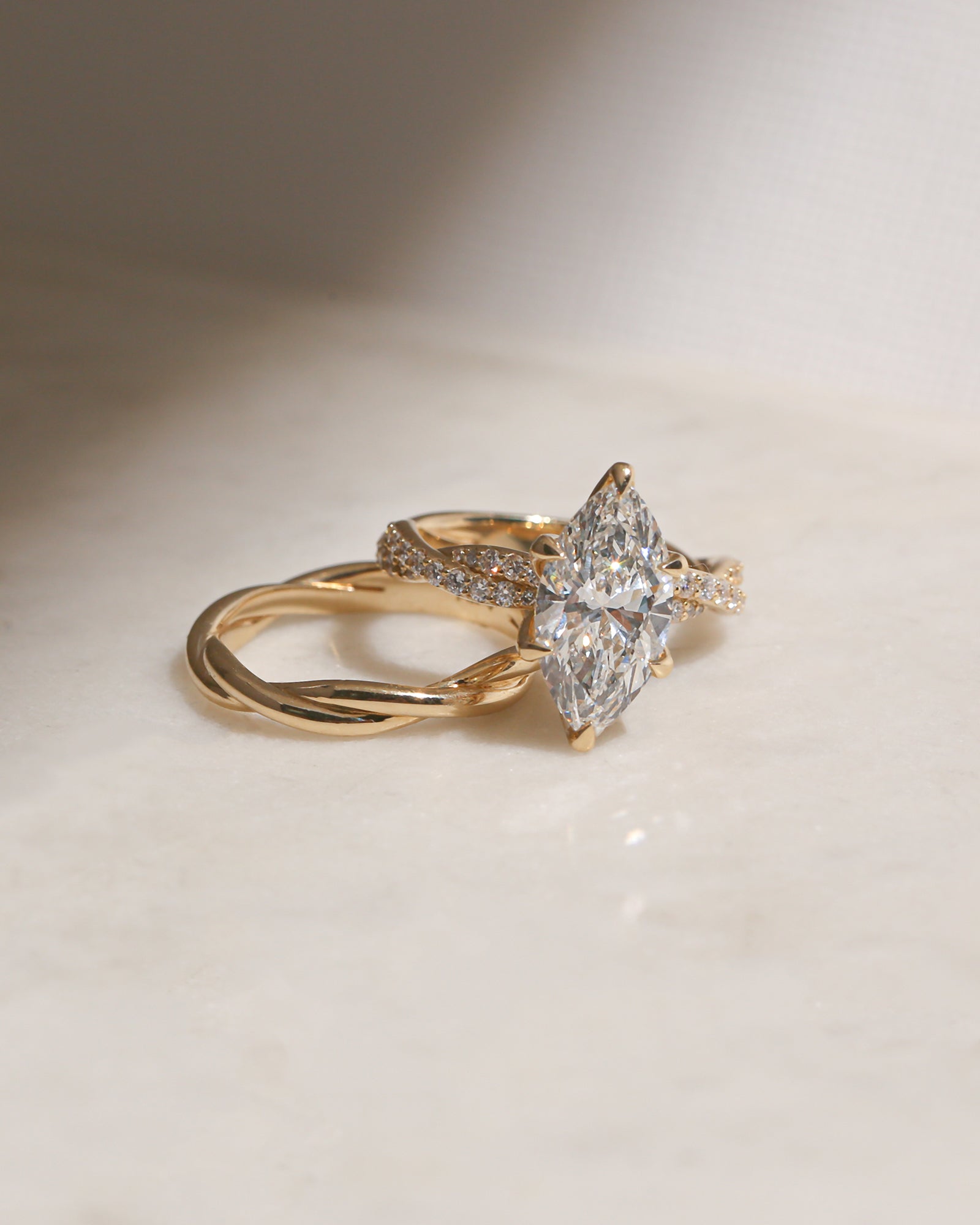 3.5 Carat Lab Grown Diamond Marquise Double Helix Ring Solid 14k Yellow Gold hovering over the Plain Gold Helix Wedding Band - lifestyle image resting on a table in indirect sunlight