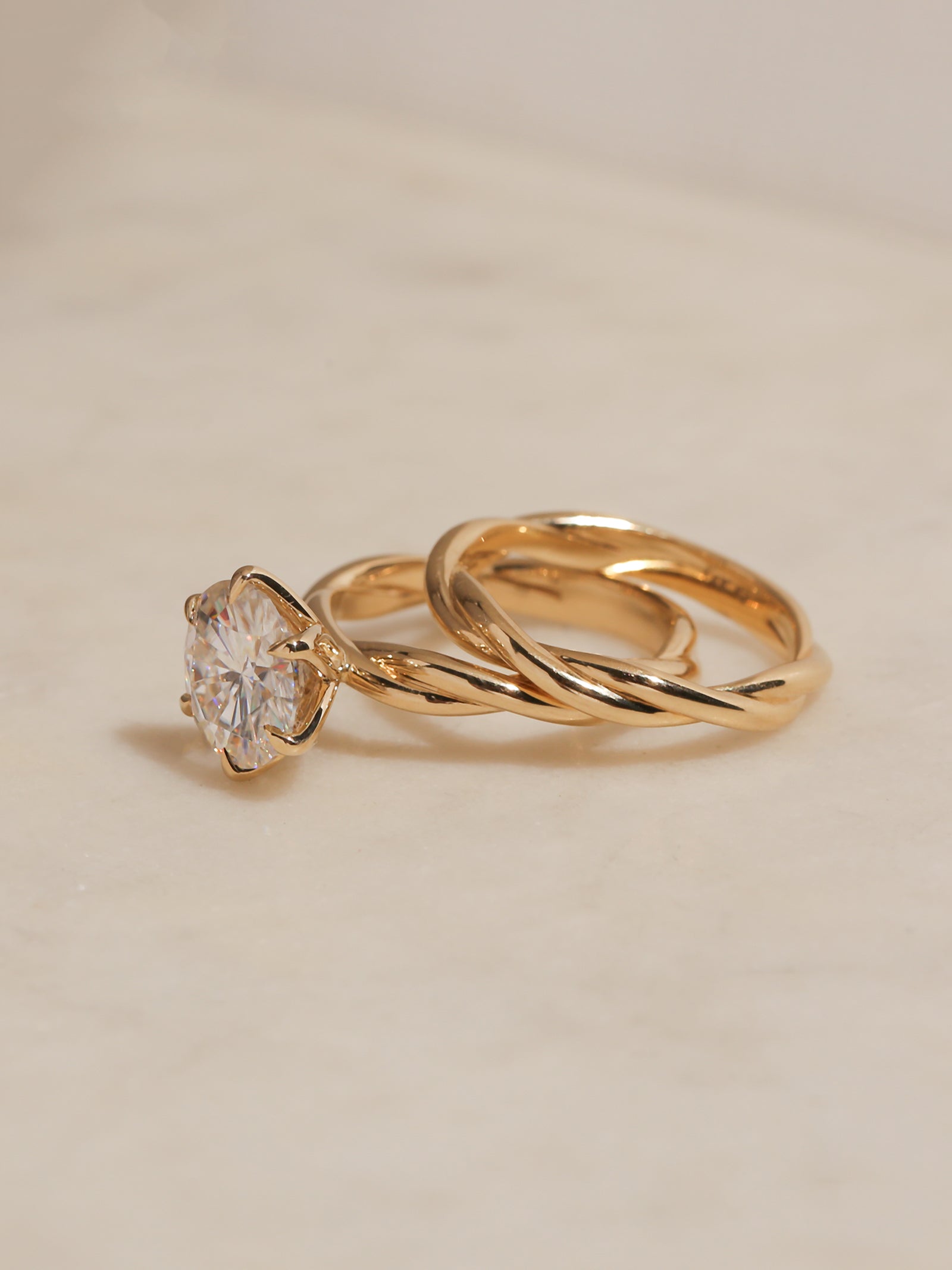 Yellow gold solitaire ring with a round diamond center and a twisted gold band, displayed on a light beige marble surface.