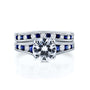 A solid 14k white gold engagement ring and wedding band set with a large round brilliant-cut center moissanite, channel-set round white diamonds and deep blue sapphires