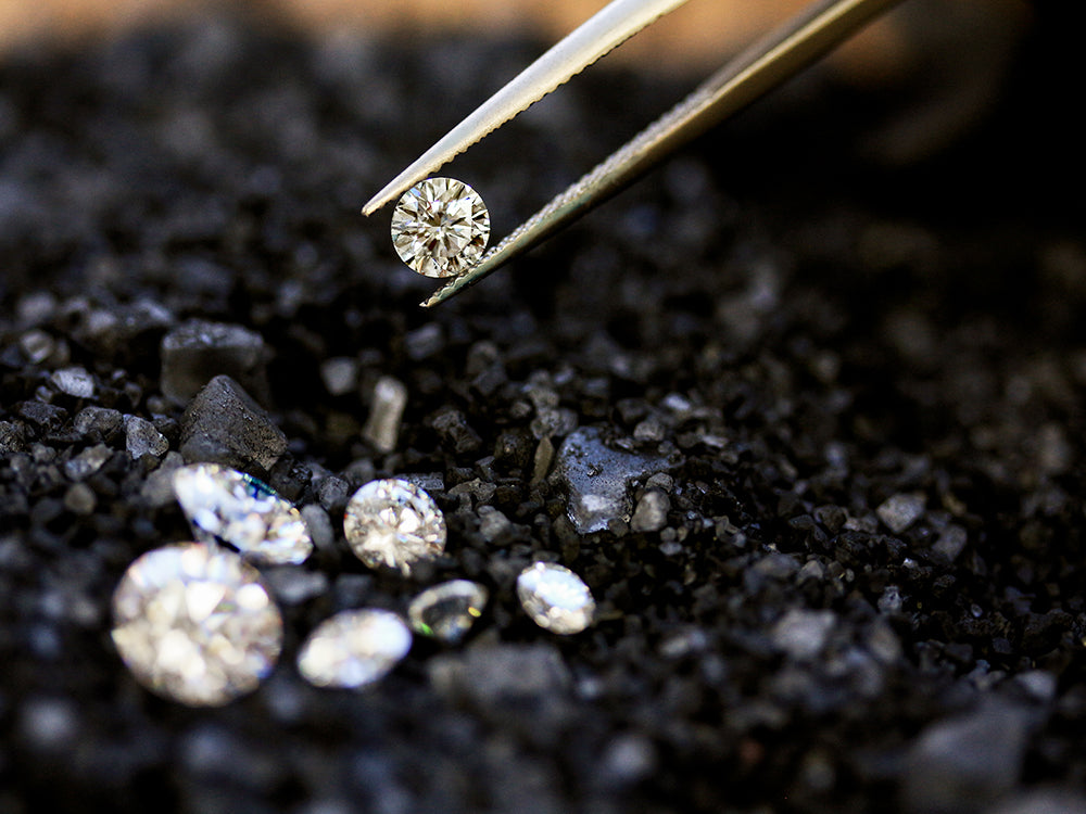 bright white diamonds on contrasting black carbon rocks with one round diamond being lifted with tweezers